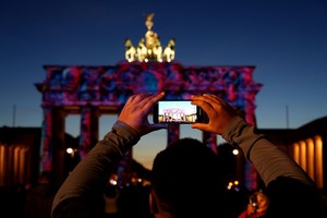 10月7日，在德國柏林，一名遊客拍攝被燈光點亮的勃蘭登堡門。（圖：新華社）