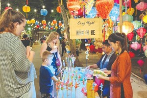 Foreign tourists visit a stall selling a traditional craft product of To He, toy figures that are made of rice dough, at the fetsival. (Photo: SGGP)