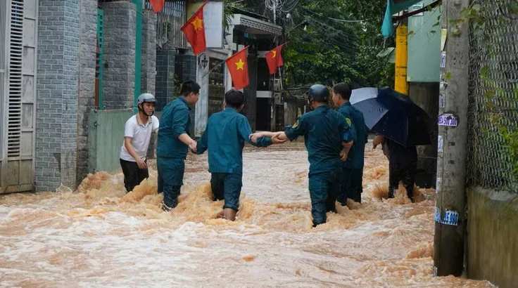 Lực lượng dân quân phường Phước Tân, thành phố Đồng Nai cố băng qua dòng nước chảy xiết để hỗ trợ người dân. (Ảnh: Lê Xuân/TTXVN)