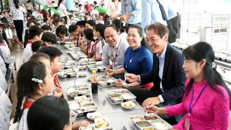Ông Koichi Ozaki, Tổng Giám đốc Ajinomoto Việt Nam (mặc vest) dùng bữa trưa theo thực đơn của Dự án Bữa ăn học đường cùng học sinh. (Nguồn ảnh: A Lộc)