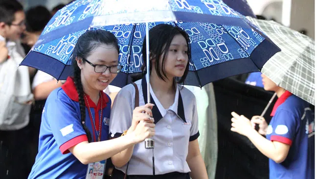 Các tình nguyện viên tại TPHCM hỗ trợ thí sinh vào phòng thi trong cơn mưa chiều 23-6 tại Hội đồng thi Trường THPT Marie Curie. Ảnh: HOÀNG HÙNG