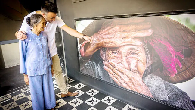 ​ Réhahn và bà Xong bên tác phẩm “Nụ cười ẩn giấu” tại buổi ra mắt phòng ảnh nghệ thuật ở TPHCM