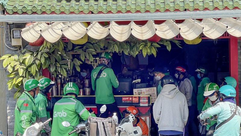 在胡志明市庆会坊孙诞街一家商店，网约车司机等候领取顾客通过应用程式订购的餐食。图：黄雄
