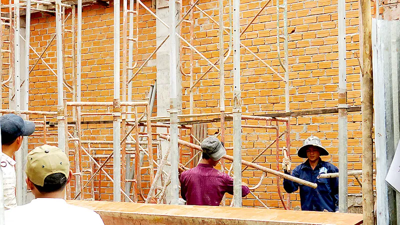 Công nhân xây dựng làm việc dưới giàn giáo nhưng không được trang bị đồ bảo hộ. Ảnh: THÁI PHƯƠNG