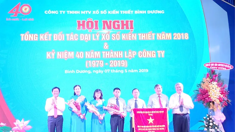 Ông Nguyễn Hoàng Thao (bìa trái), Phó Bí thư Thường trực Tỉnh ủy và ông Đặng Minh Hưng (bìa phải), Phó Chủ tịch UBND tỉnh trao Cờ thi đua của Thủ tướng Chính phủ cho Công ty TNHH MTV Xổ số kiến thiết Bình Dương