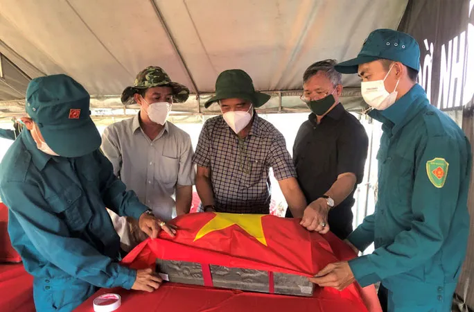 Ông Cao Tiến Dũng cùng thành viên Ban Chỉ đạo 515 phủ Quốc kỳ lên quách hài cốt liệt sĩ. Ảnh: NLĐ