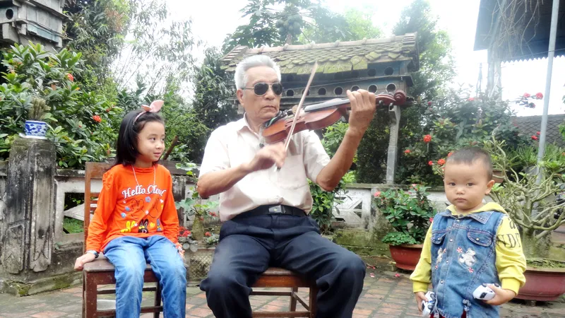 Chú Nguyễn Đăng Khoa ngồi kéo violon trước sân nhà