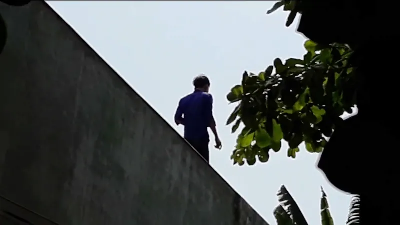 Nam thanh niên nghi ngáo đá cố thủ trên mái nhà dân. Ảnh cắt clip 