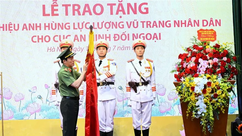 Bộ trưởng Lương Tam Quang trân trọng gắn danh hiệu Anh hùng lực lượng vũ trang nhân dân lên lá cờ truyền thống của Cục An ninh đối ngoại. Ảnh: Cổng thông tin Bộ Công an