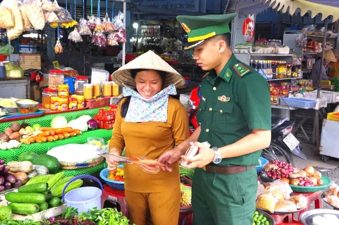 Lieutenant Tran Thanh Luat, Captain of the Mass Mobilization Team at the Tinh Bien International Border Gate Guard Station, is distributing legal advocacy leaflets to local residents (Photo: SGGP)