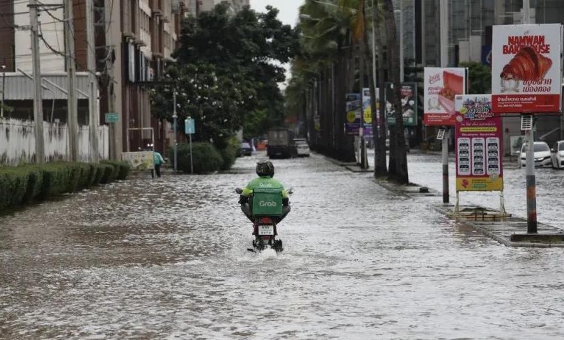 一名送货员骑车经过泰国暖武里府蒙通他尼地区一条积水道路。图片来源：BANGKOK POST