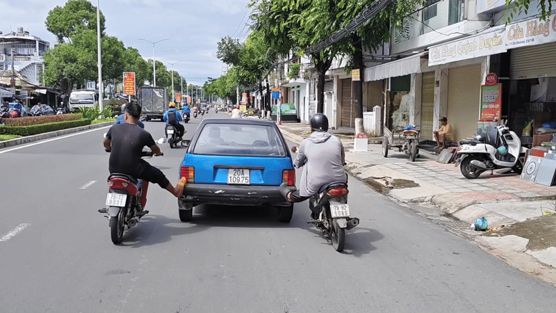 Hai người đàn ông dùng chân đẩy ô tô chạy trên đường ở Nha Trang