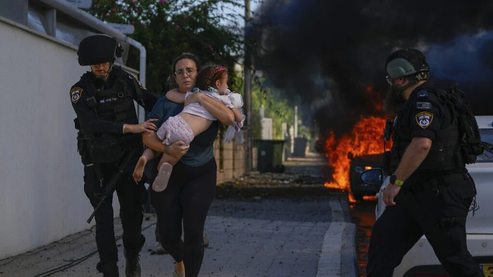 Cảnh sát đưa một phụ nữ bế con chạy ra khỏi khu vực bị tấn công bằng rocket ở Dải Gaza ngày 7-10. (Nguồn: AP)