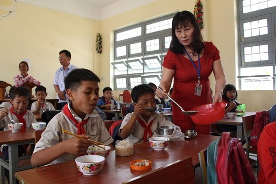 A teacher give meal portion to children (Photo: SGGP)