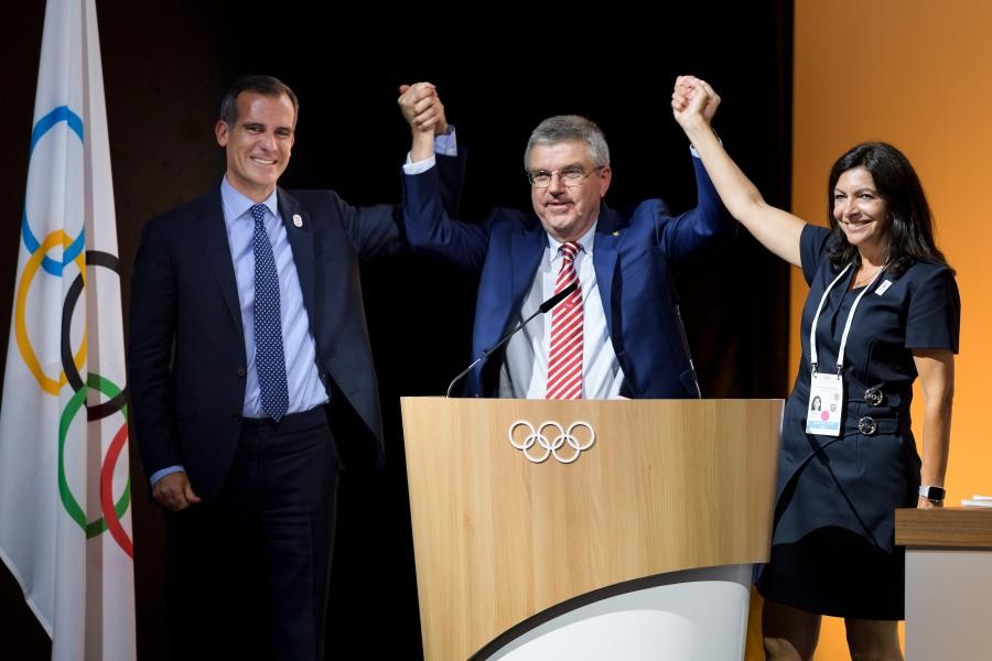 國際奧委會主席巴赫站在中間高舉兩國代表的手表示慶祝。（圖源：互聯網）