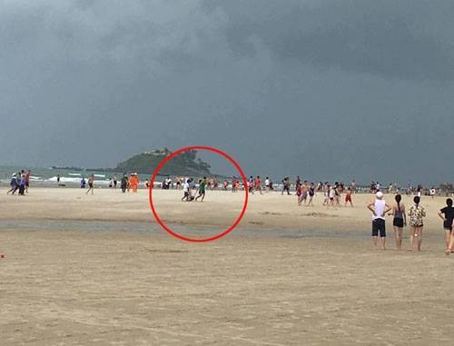 黎謙攝影師(紅圈)正在海灘為一名女遊客拍照時，突然被雷擊中。（圖源:視頻截圖）