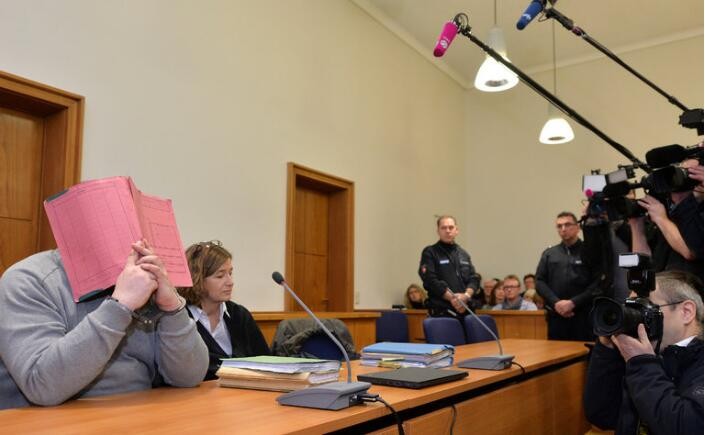 德國男護士在2014年的受審畫面，以書掩面。（圖源：互聯網）