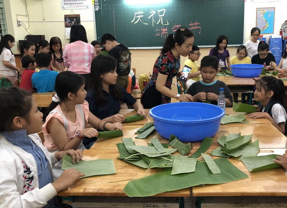 天恩外語中心老師們教小朋友使用蕉葉編織小船、粽子模型。