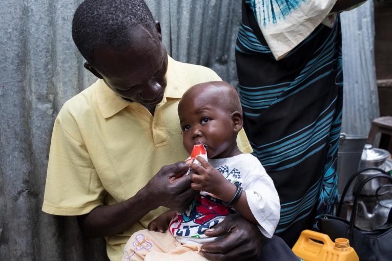 在南蘇丹首都朱巴，28歲的父親尤薩·奧古斯蒂諾（Yosa Augustino）回家後給一歲7個月的孩子吉福特（Gift）餵食高營養花生醬。（圖源：UNICEF））