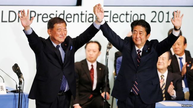 日本首相安倍晉三（右）在東京自民黨總部再次當選該黨領袖後與前國防部長石破茂舉起雙手。 （圖源：路透社）