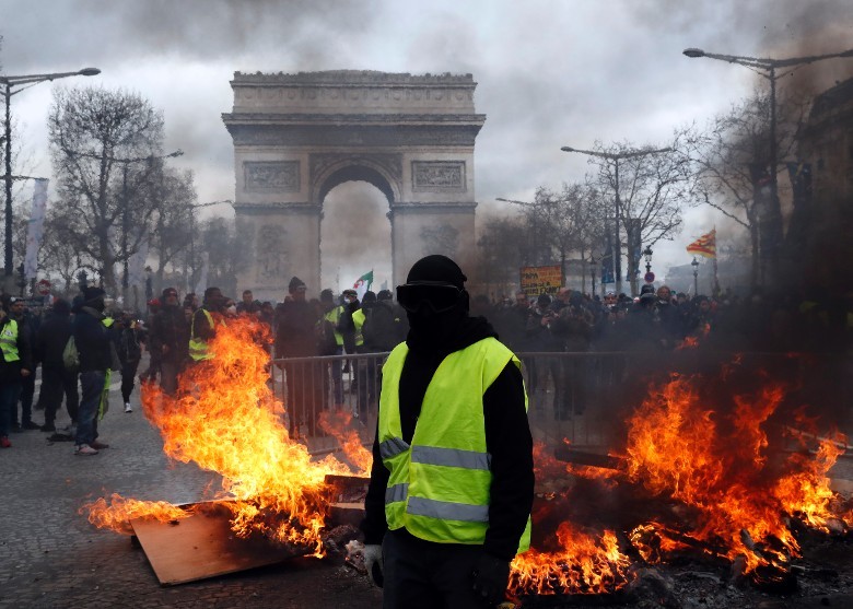 黃背心示威者站在凱旋門和被焚燒雜物前面。（圖源：AP）