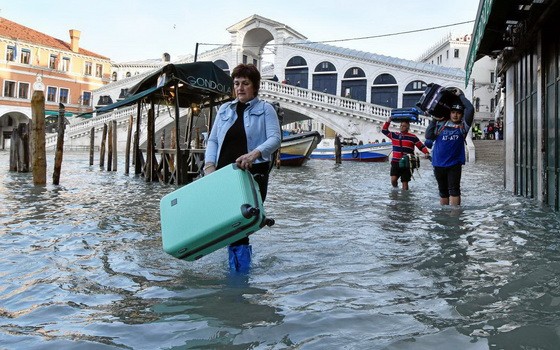 當地時間12月23日，意大利威尼斯的里亞托橋附近，一名女性拎著箱子涉水而行。 （圖源：路透社）