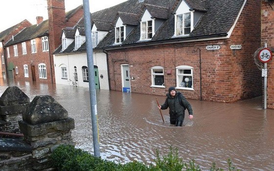 英國西部滕伯里威爾斯特梅河決堤造成街道淹水，一名男子週日涉水越過道路。（圖源：AFP）