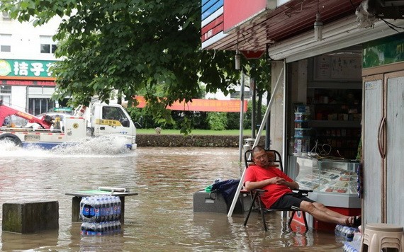 圖為浙江衢州6月30日因大雨導致路面積水，不過當地一名男子仍淡定地在自家雜貨店門口打盹。（圖源：路透社）
