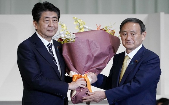日本內閣官房長官菅義偉（右）當選自民黨新總裁後向安倍晉三獻花。（圖源：AFP）