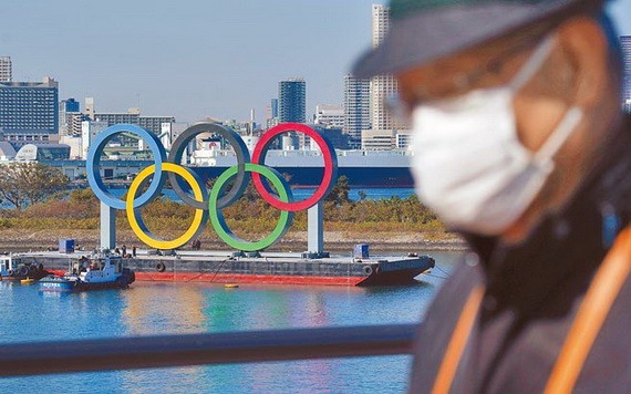 一名戴口罩的男子在奧運五環背景中行走。（圖源：AP）