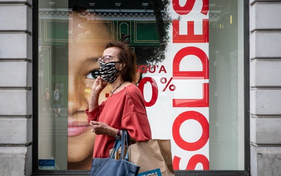 7月15日，一名女子戴口罩走過法國巴黎街頭一處打折季的廣告牌。（圖源：新華社）