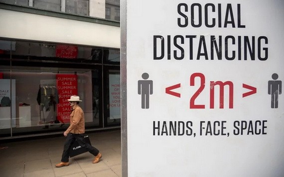 圖為英國倫敦一名男子從提示人們保持社交距離的牌子旁走過。（圖源：新華社）