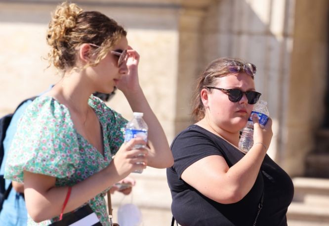圖為7月13日，在法國巴黎盧浮宮博物館玻璃金字塔廣場上，一名女子把冰鎮礦泉水貼在臉上解暑。（圖：新華社）