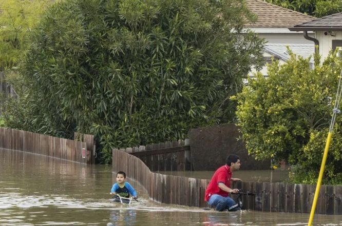 人们骑着自行车穿过洪水。（图：AP）