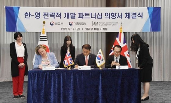 5月12日，在首尔外交部大楼，韩国企划财政部第一次官（副部长）方基善（中）、外交部第二次官李度勋（右）同到访的英国外交、联邦和发展事务部负责印太事务的国务大臣安妮-玛丽·特里维廉（左）签署《关于韩英建立战略发展合作关系的意向书》。（图：韩联社）
