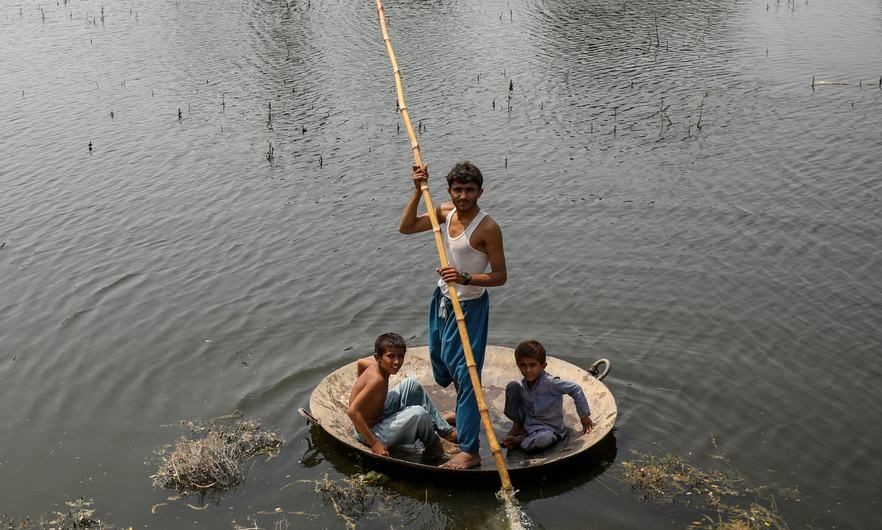 在巴基斯坦信德省，男孩们用一个大平底锅作为临时筏子趟过洪水。（图：联合国）