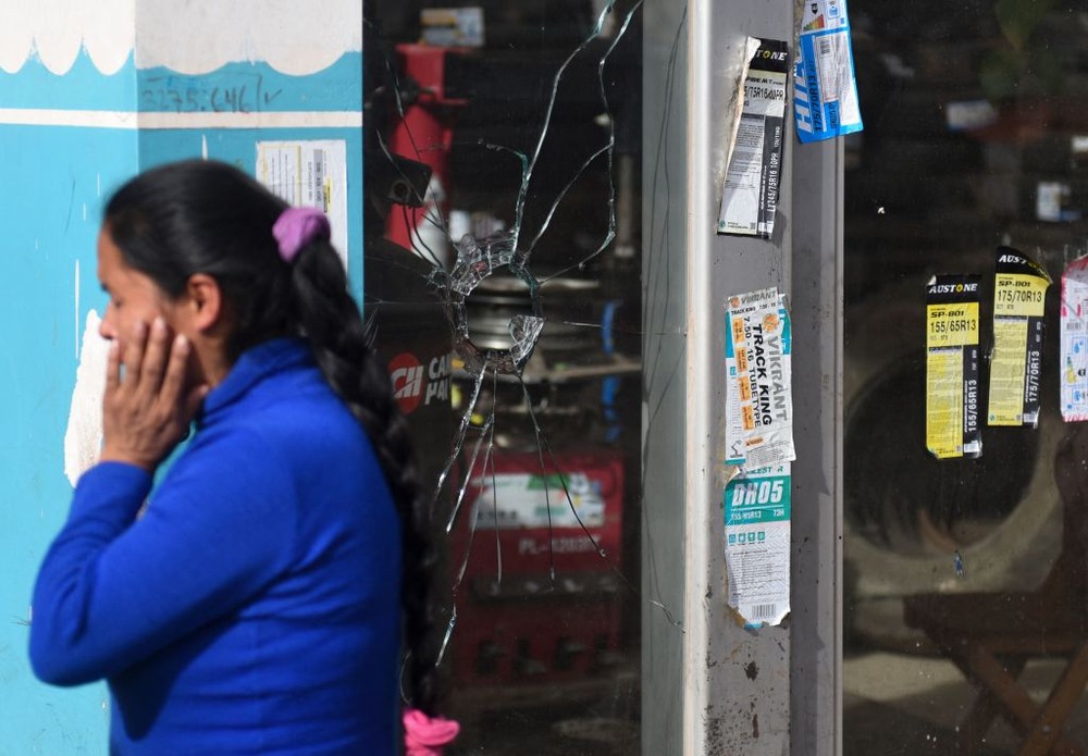 图为2023年1月19日，在秘鲁安第斯山脉城市库斯科，警察击退了占领机场场地的抗议者，一名妇女在一块被弹丸击碎的玻璃旁讲电话。（图：Getty Images）