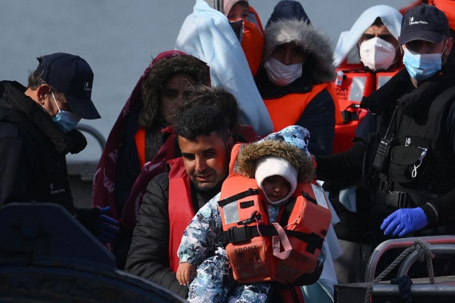 图为2022年5月3日，在多佛港码头，试图穿越英吉利海峡的移民被英国边境部队一名成员扶助从船上走下来。 （图：AFP）