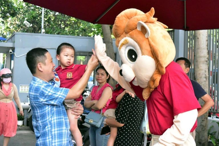 一名家长抱着幼儿园女孩返回越澳国际学校旧邑Garden Hills分校，在校门前与吉祥物扮演者碰手。（图：T.H.）