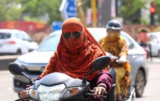 7月6日，在印度博帕尔，骑车的人们将头部包裹以遮阳防晒。（图：新华社）