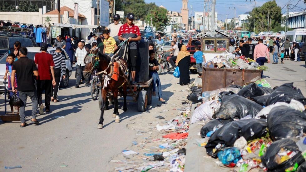 2023年10月16日，在加沙地带南部的汗尤尼斯，巴勒斯坦人从成堆的垃圾旁经过，这些垃圾有可能引发一场环境灾难。 （图：路透社）