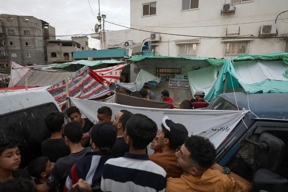 大批巴勒斯坦人16日在加沙一家医院外的一个摊位排队买面包。联合国多次警告加沙的人道主义局势严峻，以色列已宣布“全面包围”加沙，切断基本供应报复哈马斯10月7日的突袭。（图：AFP）