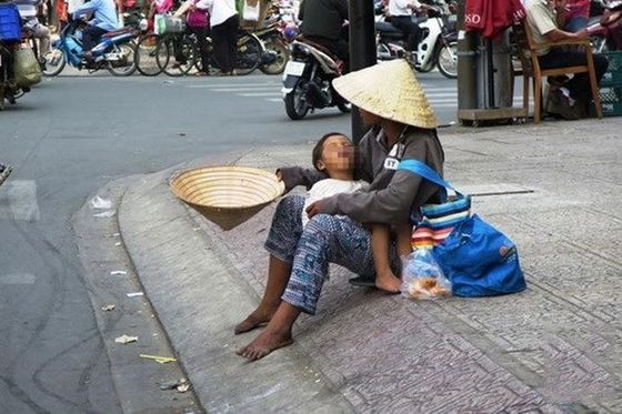 一名乞丐抱着小孩坐在路旁行乞。（示意图：越通社）