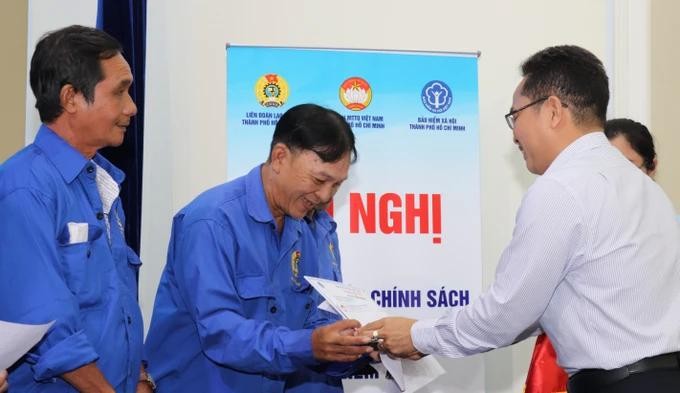 市越南祖国阵线委员会副主席范明（右）向贫困者颁赠社保册。（图：红海）