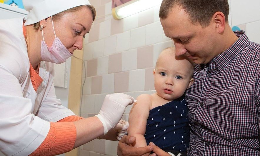 一名婴儿被父亲抱在怀中，接受护士接种的第一剂麻疹、腮腺炎和风疹三联疫苗。（图：儿基金）