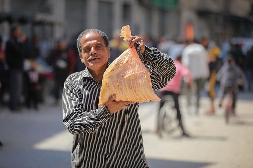 4月14日，一名男子在加沙城领取完大饼后回家。
