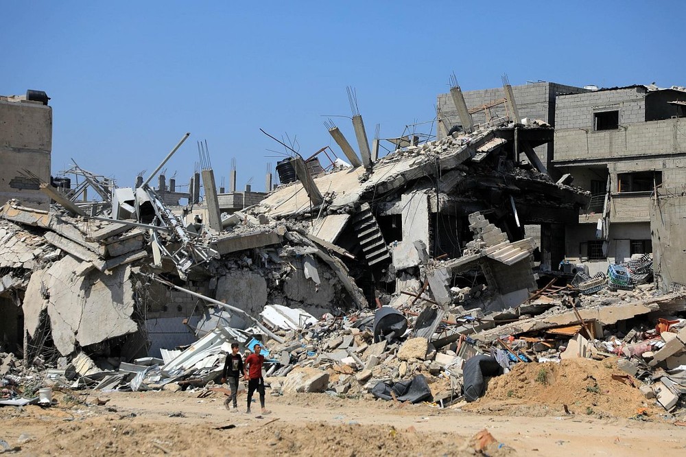 在加沙地带南部城市汗尤尼斯，人们走过损毁的建筑。（图：新华社）