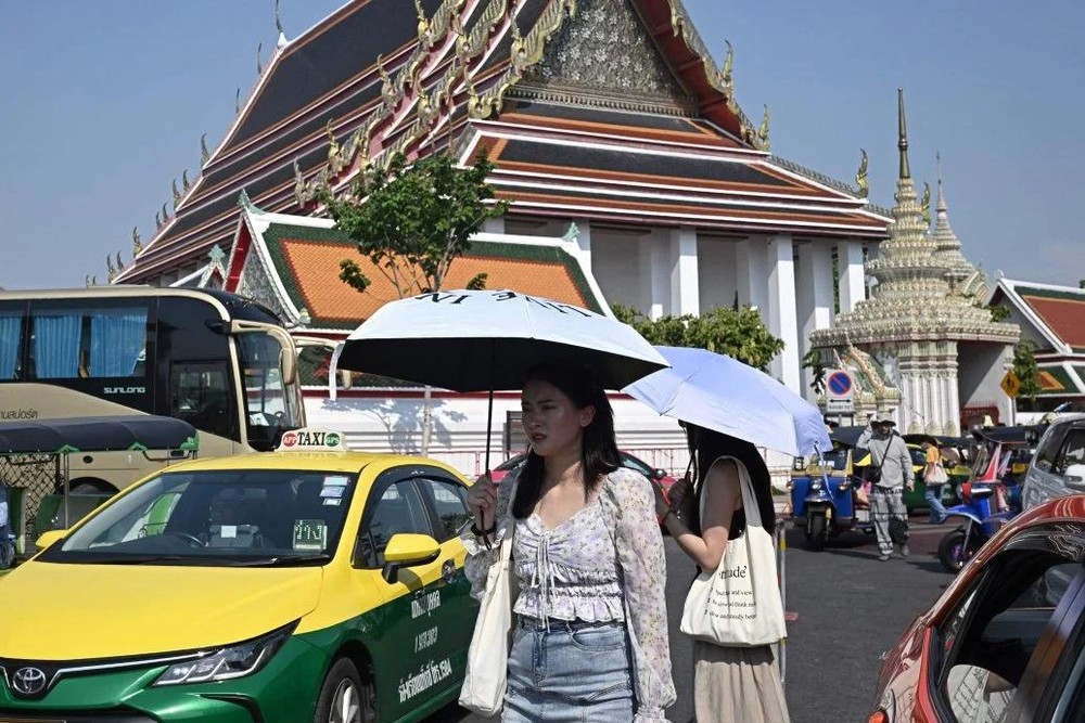 曼谷的极端高温未让游客却步，许多游客撑伞在曼谷卧佛寺溜达。（图：AFP）
