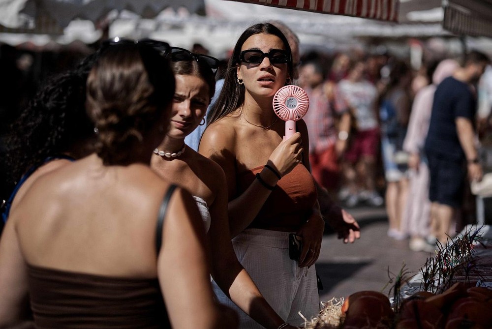 图为2023年8月22日，在法国南部城市尼斯街头，一名女子用小风扇降温。（图：新华社）