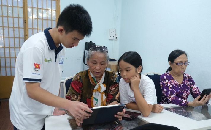 天资高中学校十年级学生晋勇正在指引杨氏蓉老大娘与其孙女使用智能手机、平板电脑上的应用程式。